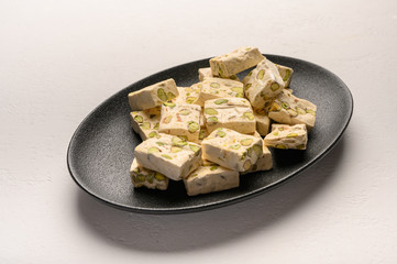 Eastern Arabic nougat sweetness with pistachios on a black ceramic plate on a light background