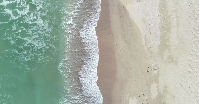 Static top down view of tropical beach, foamy ocean waves washing sand. Waves hitting sand beach