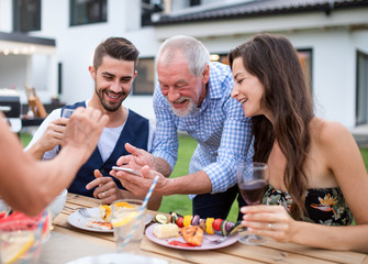 Portrait of people outdoors on family garden barbecue, taking selfie.