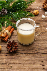 Christmas eggnog liqueur or cola de mono cocktail. Classical winter drink in glass mug, xmas decorations. Evergreen branches, cinnamon, walnuts, sugar. Old wooden background