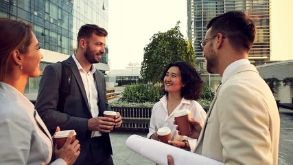 Group of coworkers having a coffee brake together, standing outside in front of office buildings and talking. - Powered by Adobe