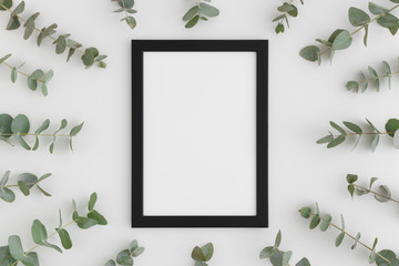Top view of a black frame mockup surrounded by branches of eucalyptus on a white background.