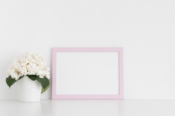 Pink frame mockup with a hortensia in a pot on a white table.Landscape orientation.