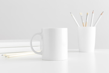 Mug mockup with workspace accessories on a white table.