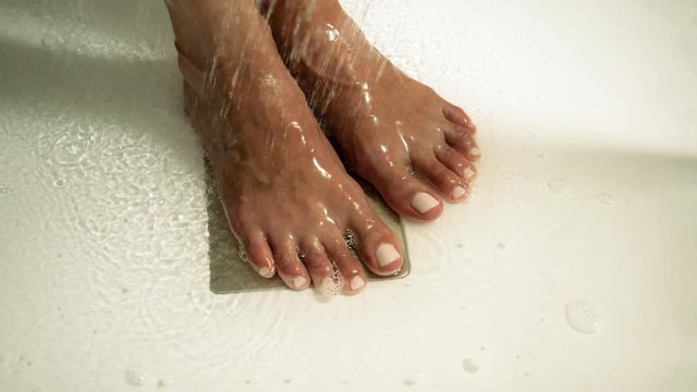 Young beautiful woman taking a shower in a bathroom. Close-up shot of female legs. Slow motion. HD
