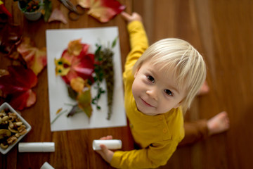 Sweet child, toddler boy, applying leaves using glue