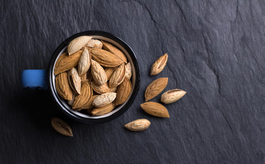 Mug with garden and mountain almonds in shell on black slate background, top view, free space