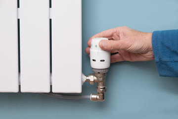Hand turning down temperature on TRV radiator thermostat valve
