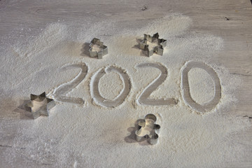year 2020 written by hand on flour surface with cookie cutters in shape of a man, a fir tree, a star and a snowflake