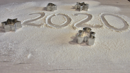 year 2020 written by hand on flour surface with cookie cutters in shape of a man, a fir tree, a star and a snowflake
