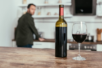 Selective focus of wine glass with bottle on table and man on kitchen