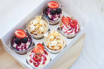Mousse desserts in cup with cream cheese frosting, berry sauce, salted caramel, strawberry, cherry, raspberry and popcorn. 