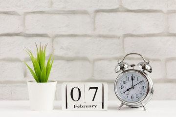 February 7 on a white wooden calendar next to the alarm clock, on a light background.