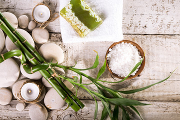 Grean bamboo leaves, soap bar, towel and candles over zen stones on white wooden background. Top view