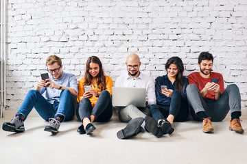 University students sitting on floor in classroom using mobile devices