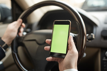 Close-up of young man holding mobile phone with blank screen in his hand he using navigator during driving