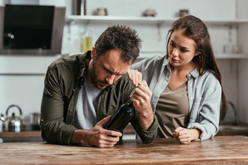 Woman supporting alcohol addiction husband with wine bottle on kitchen