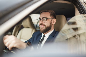 Successful young businessman in eyeglasses driving his car and smiling