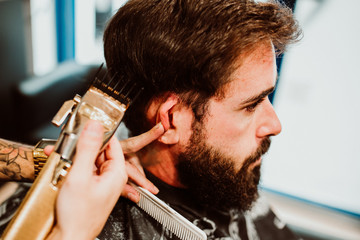 .Young hipster man with hearty beard cutting his hair in a barbershop. Professional hairdressing work. Lifestyle..