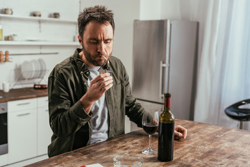 Alcohol addicted man lighting cigarette beside wine on table