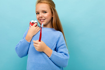 young european girl holds a toothbrush and jaw in her hands on a light blue background
