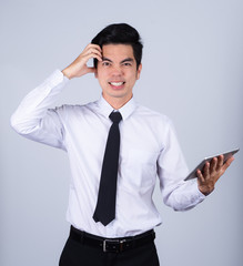 Portrait handsome young asian man wearing a white shirt holding smart phone or tablet stressed and anxiety isolated on gray background in studio. Asian man people. business success concept.