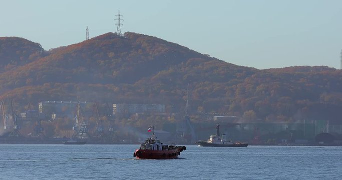 City of Nakhodka. A small red tugboat goes on Nakhodka Bay on the background of coal ports