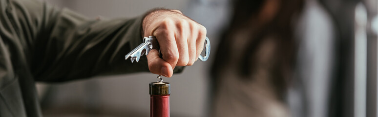 Selective focus of man opening wine bottle and worried wife at background, panoramic shot