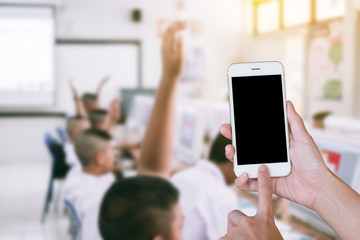 Hands woman are holding touch screen smart phone,tablet on blurred classroom computer with student and teacher background.