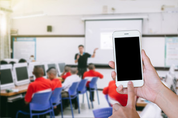 Hands woman are holding touch screen smart phone,tablet on blurred classroom computer with student and teacher background.