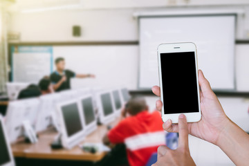 Hands woman are holding touch screen smart phone,tablet on blurred classroom computer with student and teacher background.