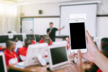 Hands woman are holding touch screen smart phone,tablet on blurred classroom computer with student and teacher background.
