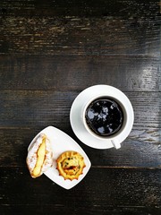 One small croissant with vanilla cream and cheese pastry with chocolate pieces served in white plate with black filtered coffee for a traditional greek breakfast