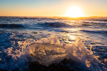 Iceberg melting at sunrise on black volcano beach of Jökulsárlón glacier lagoon, Iceland