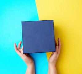 two female hands hold a closed dark blue paper cardboard box