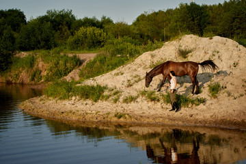 young woman led a horse to a watering hole at sunset