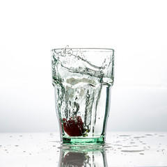 In the glass with clean and transparent water, falls fresh strawberries, splashes water.