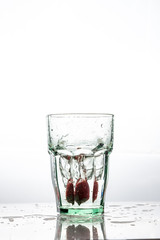 In the glass with clean and transparent water, falls fresh strawberries, splashes water.