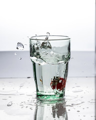 In the glass with clean and transparent water, falls fresh strawberries, splashes water.