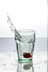 In the glass with clean and transparent water, falls fresh strawberries, splashes water.
