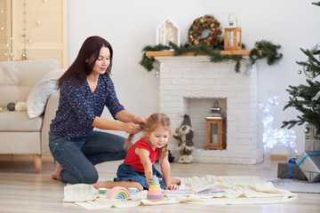 Mom and daughter are playing together in an elegant Christmas room. Christmas morning with family. New Year or Christmas interior