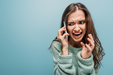 aggressive woman screaming and talking on smartphone, isolated on blue