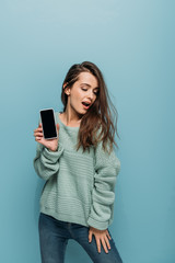 sexy woman showing smartphone with blank screen, isolated on blue