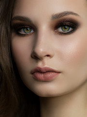 Close-up portrait of beautiful woman's purity face with dark black smoky-eyes make-up, nude full lips. Sexy model with clean shiny skin, purity complexion
