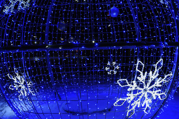 Glowing giant balls in the lights on a snowy street. New Year Christmas street decorations.