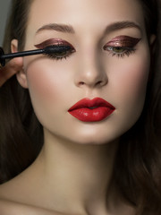 Close-up of female green eye with burgundy thick eyeliner. Mascara brush colors extra long eyelashes. Thick beautiful eyebrows and red lips. Clean smooth skin. Cosmetology and spa