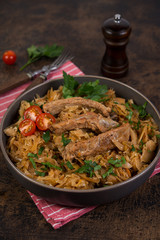 Bigos of stewed sauerkraut with pork ribs. Traditionally the Polish dish in a plate decorated with greens and tomatoes stands on a wooden table. Vertical orientation.