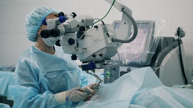 Surgeon is observing eye operation through the medical device. Ophtolmologist in eye hospital.