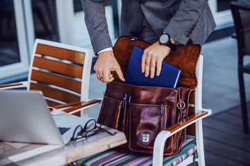 Cropped picture of elegant businessman in suit taking out agenda from his leather bag. Cafe...