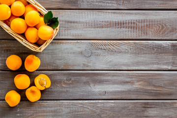 Fresh raw apricots in basket on dark wooden background top view space for text pattern with leaves